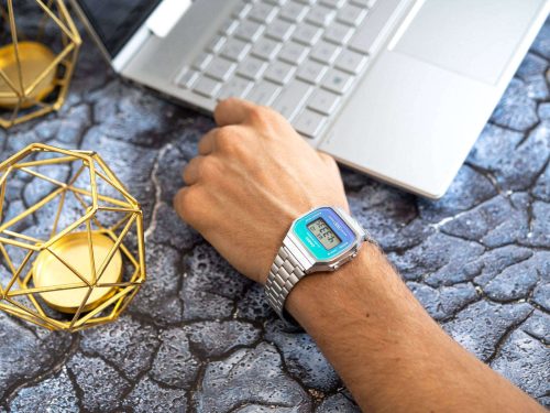 CASIO A168WER-2AEF unisex ručni sat na ruci muskarca koji radi na kompjuteru, retro dizajn sa srebrnom čeličnom narukvicom