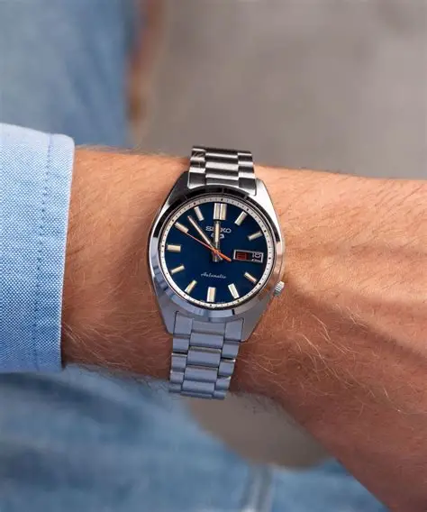 Seiko SRPK87K1 5 Sports SNXS muški sat u srebrnoj boji na ruci muškarca, prikazujući njegov elegantan dizajn sa plavim brojčanikom i čeličnom narukvicom. Savršen za svakodnevno nošenje i poslovne prilike.