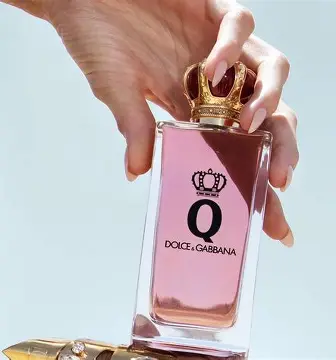 Detalj bočice Q Intense EDP sa elegantnim staklom i crveno‑zlatnim čepom u ruci zene