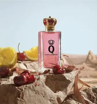 Dolce & Gabbana Q Intense EDP – lifestyle fotografija sa parfemom na pesku, dekorativnim cvetom i mekom rasvetom