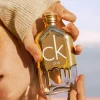 Detalj bočice Calvin Klein ONE Gold EDT sa zlatnim i minimalističkim linijama u ruci