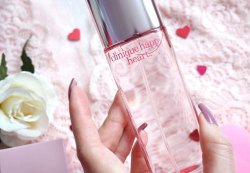 Mirisne note Clinique Happy Heart sa mandarinom, krastavcem, hijacintom, jasminom i mošusnom bazom. parfem u ruci devojke sa dugackim noktima, srca okolo.
